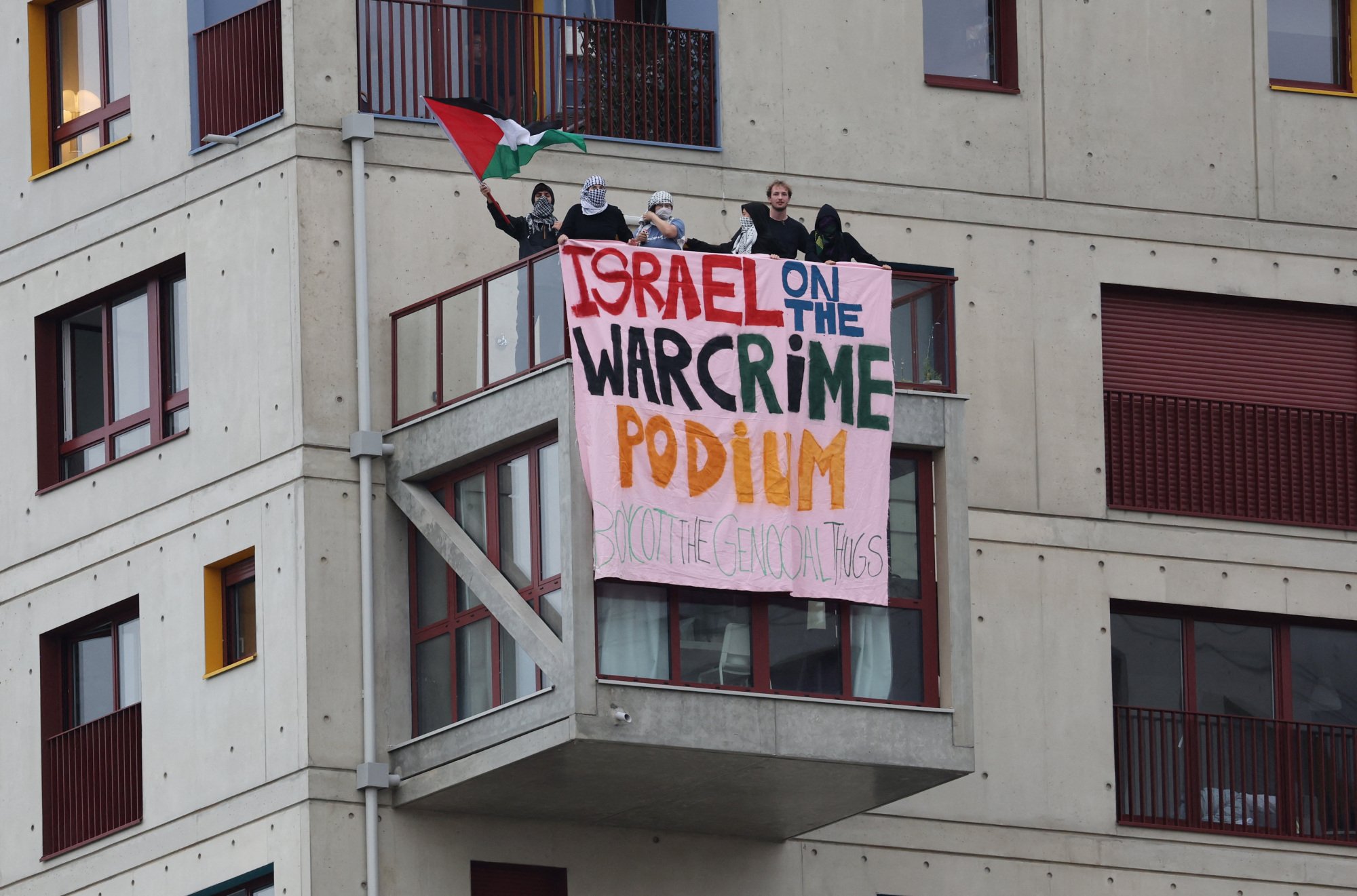 A large banner on the side of an apartment building that reads "Israel on the warcrime podium."