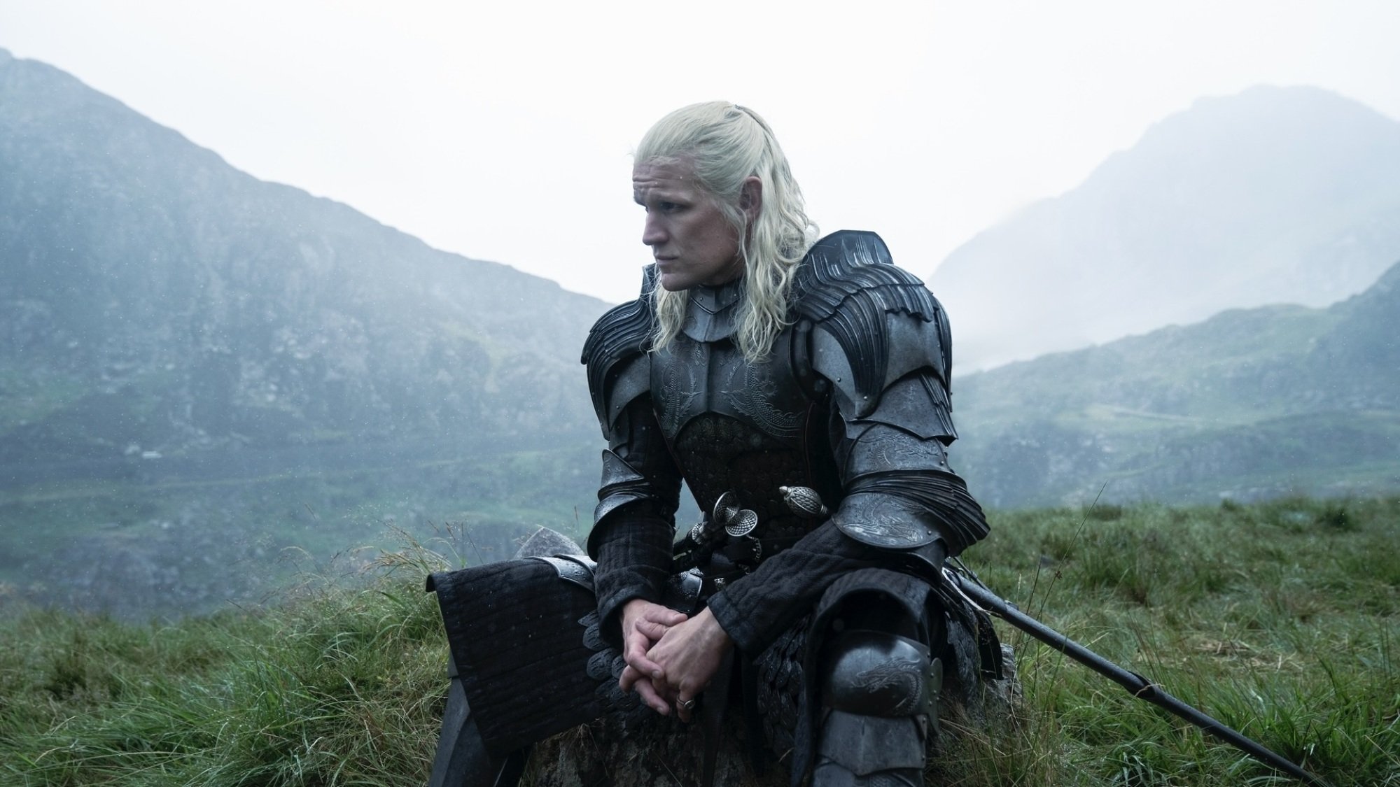 Daemon Targaryen sits in a green field in armor.