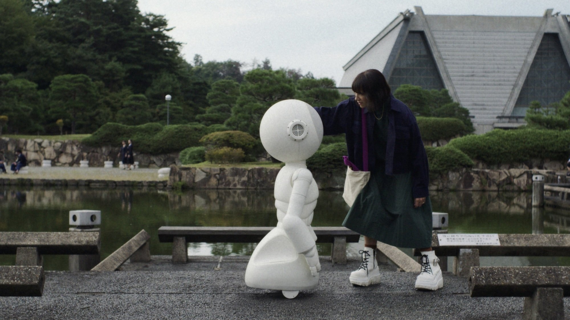 A woman touches a white robot to check if it's okay while outside in a garden.