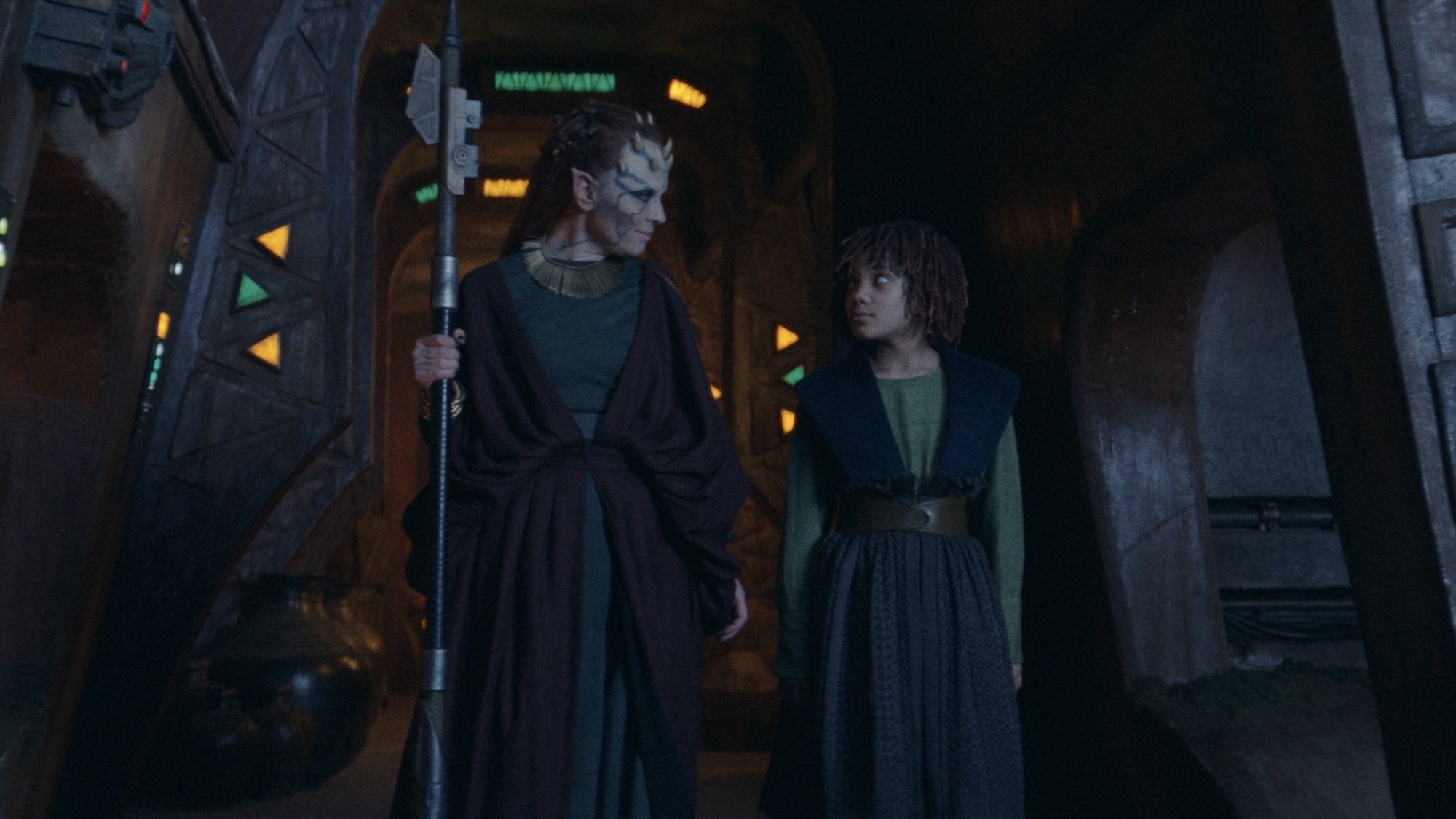 Mother Koril and young Mae walk through a dark corridor on Brendok.