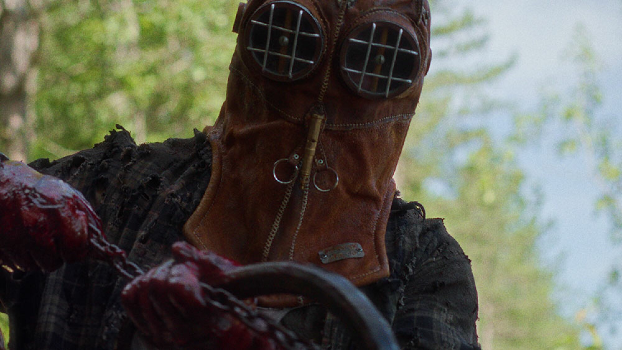 A close-up of a man with bloody hands wearing an old firefighter mask.