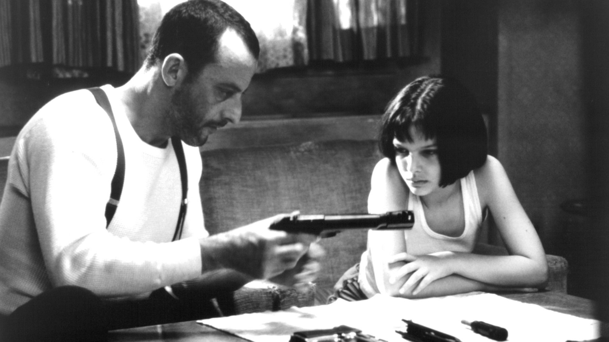 Jean Reno loads a gun in front of Natalie Portman in a scene from the film "Leon: The Professional."