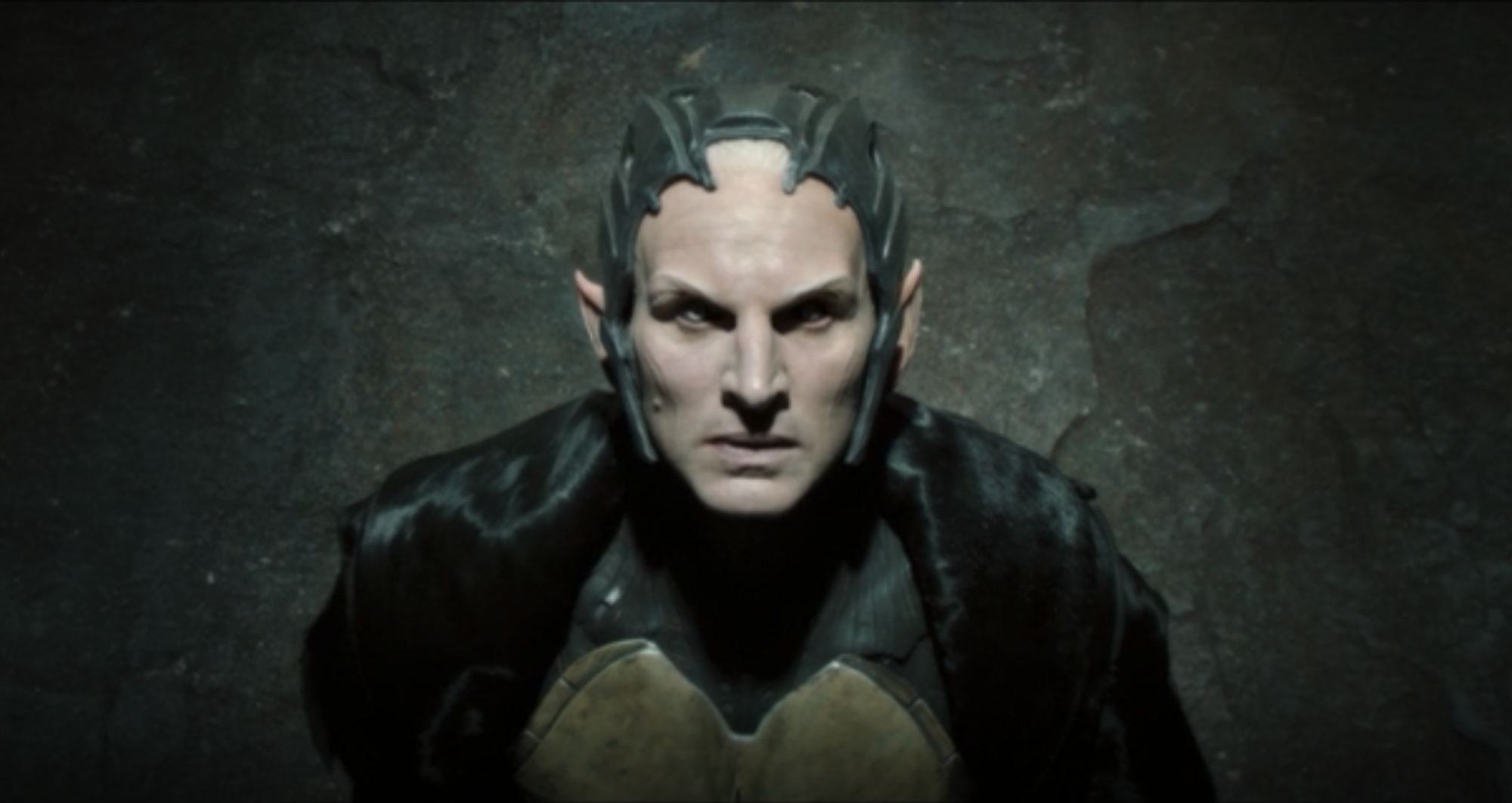 Closeup of a pale, pointed figure with a sharp metal crown and dark robes: Malekith (Christopher Eccleston), the leader of the dark elves.