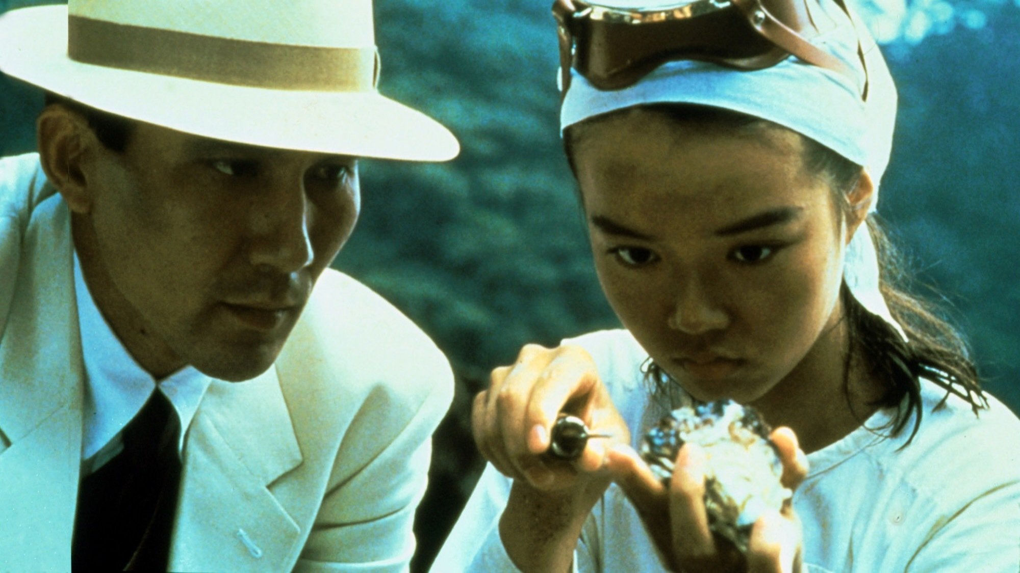 A Japanese man in a hat watches a young oyster diver cut open an oyster.