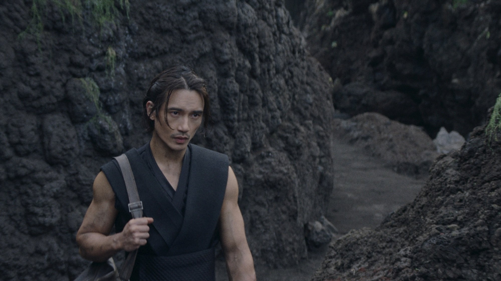 The Stranger walks down to the beach in an all-black outfit.