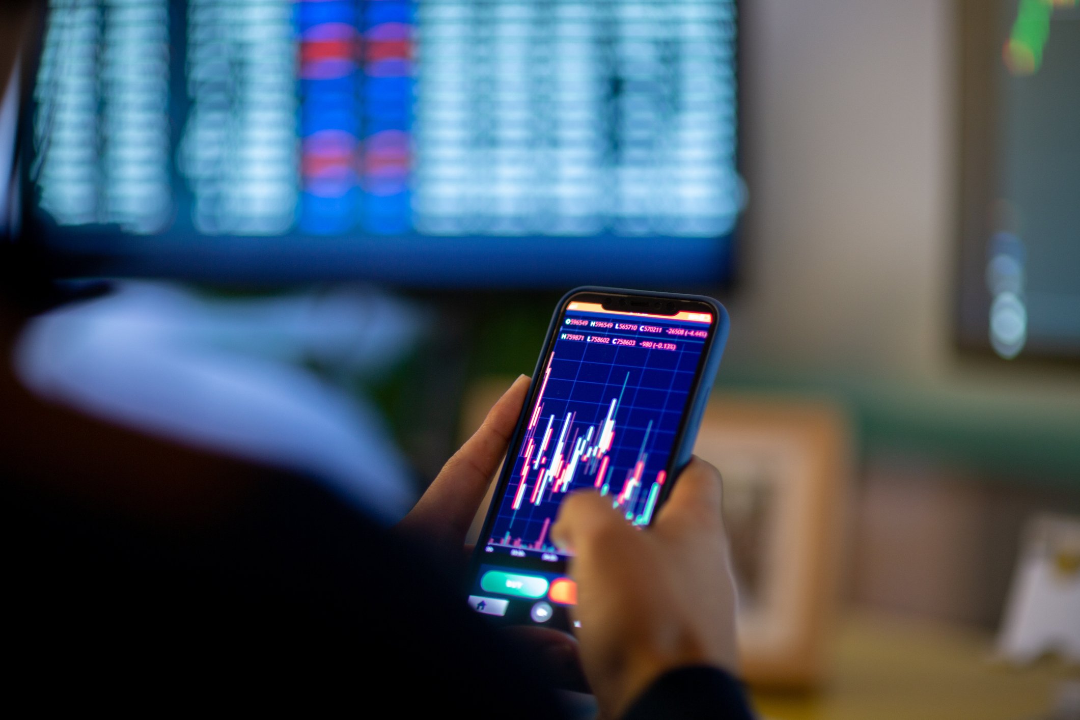 Man looking at currency trading app on his smart phone from his home office 