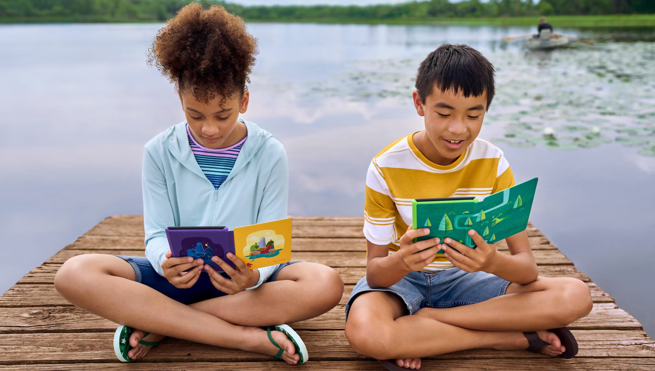 Two kids sit by the water reading their Kindles