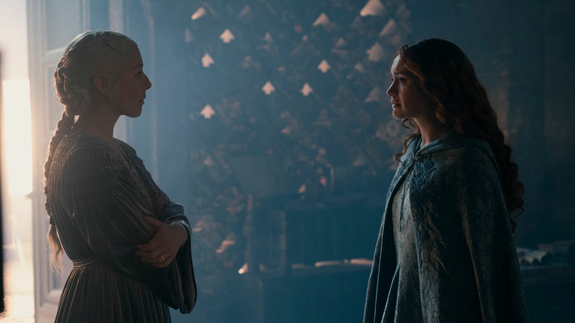 Two women in medieval clothes stand in a dark room, facing each other.