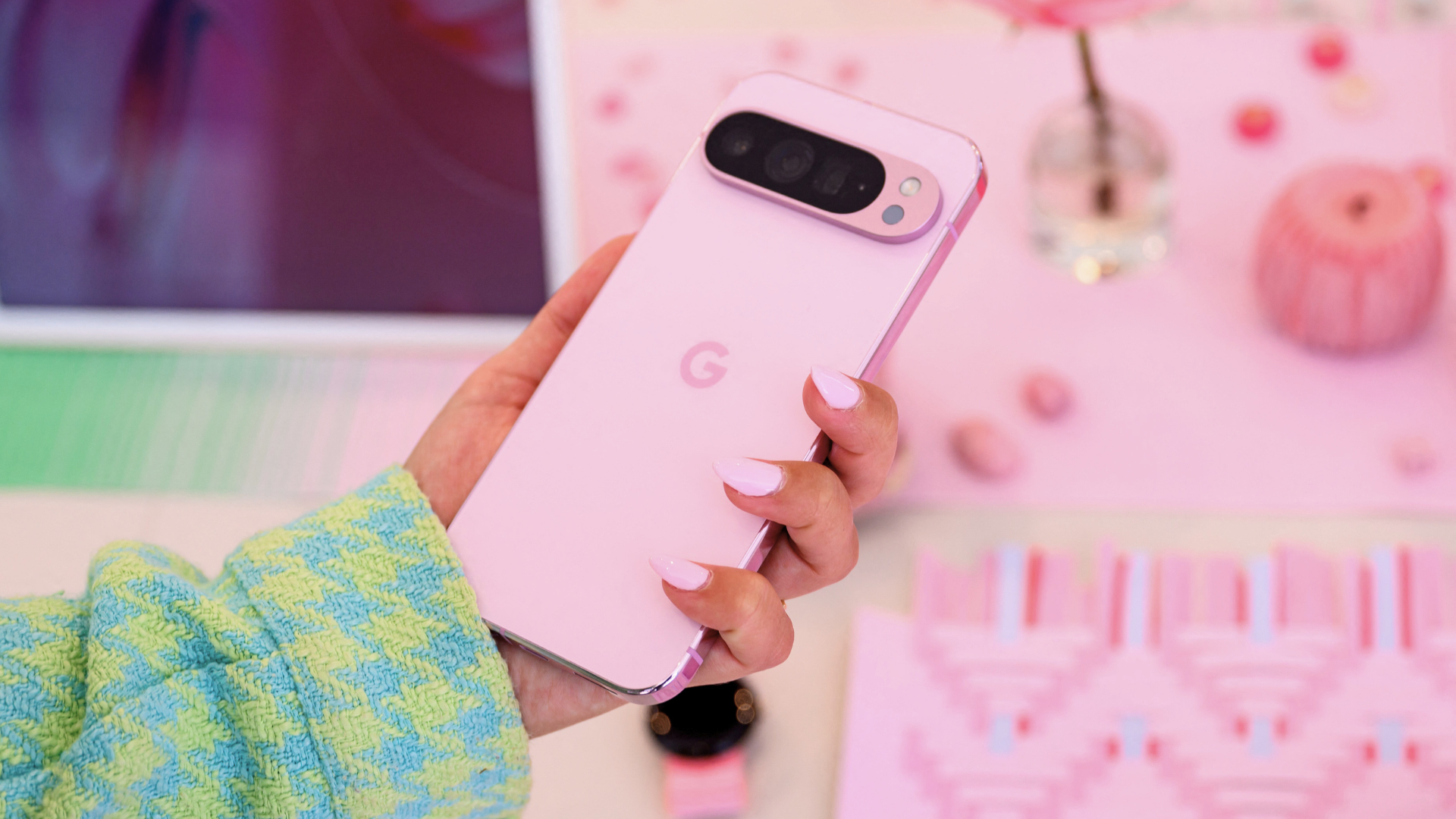 A phone with rose pink painted nails holds a rose pink Pixel 9 Pro.