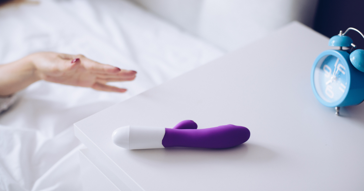 Young woman holding sex toy dildo vibrator in bed