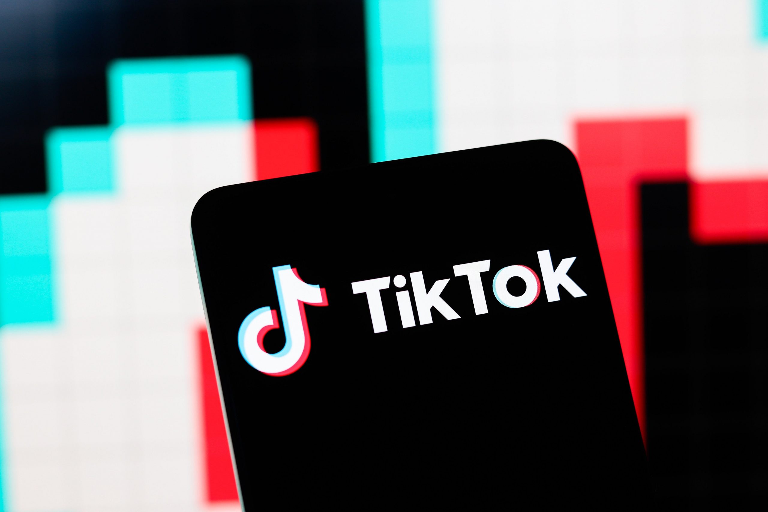 The TikTok logo displayed on a phone with the colors of TikTok, blue and pinkish red in the background.