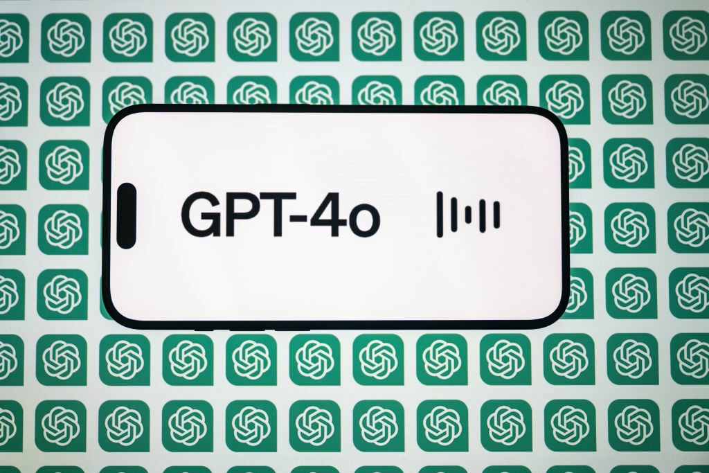  the 'Chat GPT-4o' logo is displayed on a mobile phone screen in front of a computer screen displaying the 'Chat GPT' logo