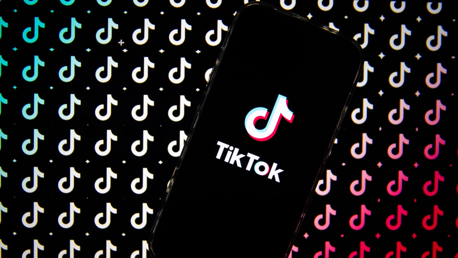 TikTok logo is displayed on a smartphone screen then replicated in pattern behind it.