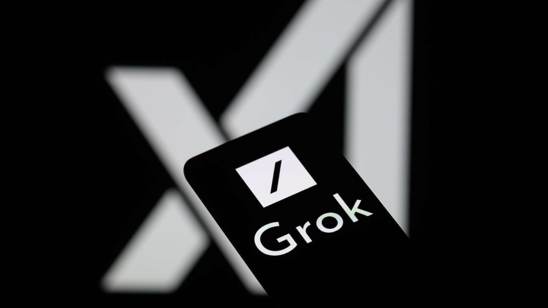 The Grok logo is being displayed on a smartphone with the X AI icon visible in the background.