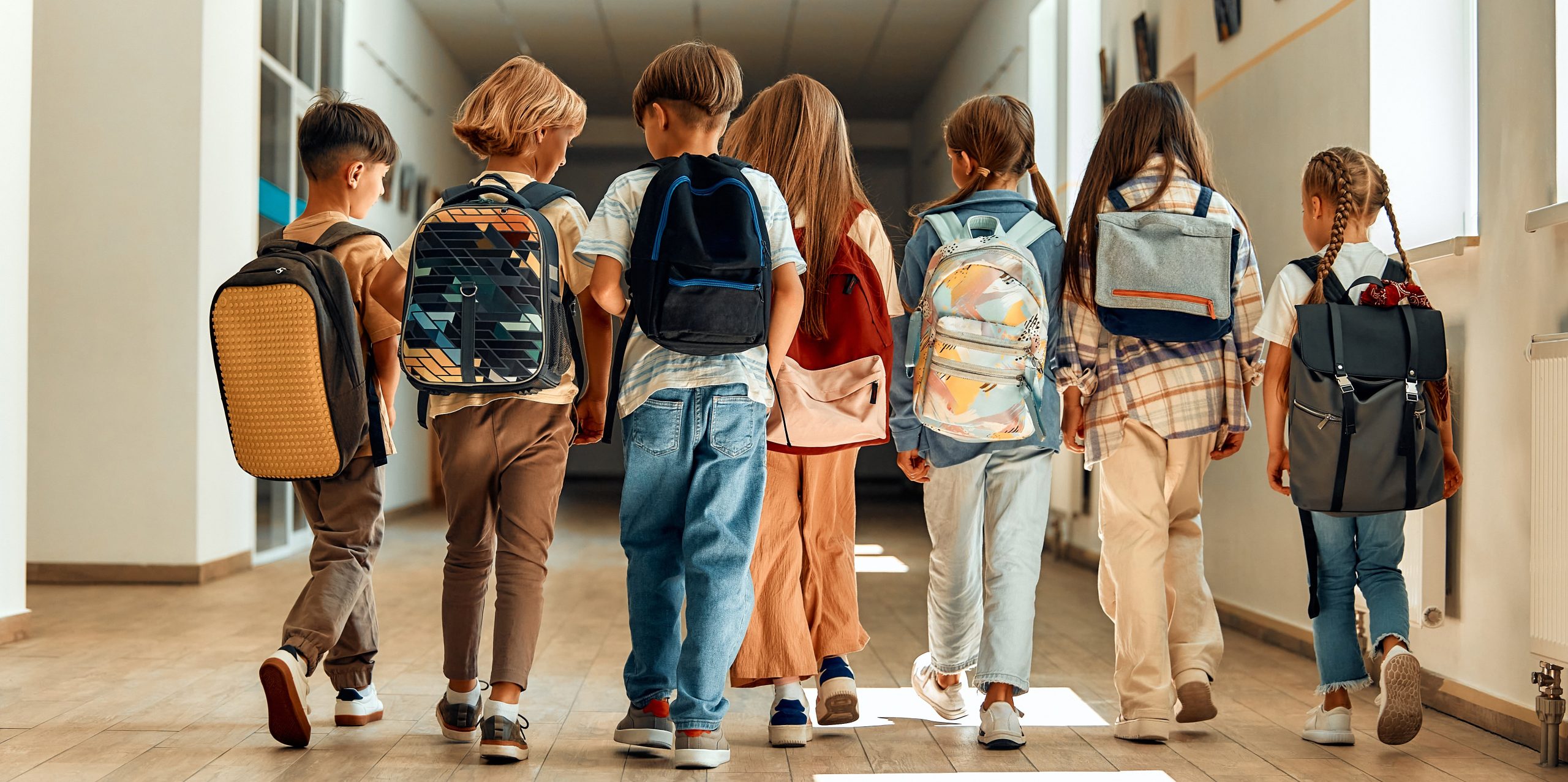 a group of school kids walk down the hallway while all wearing backpacks