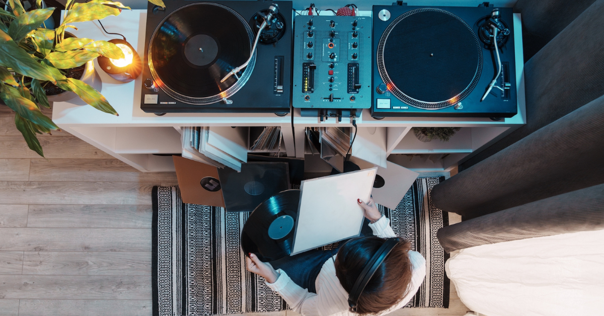 Top view of a person with headphones handling vinyl records beside a turntable.