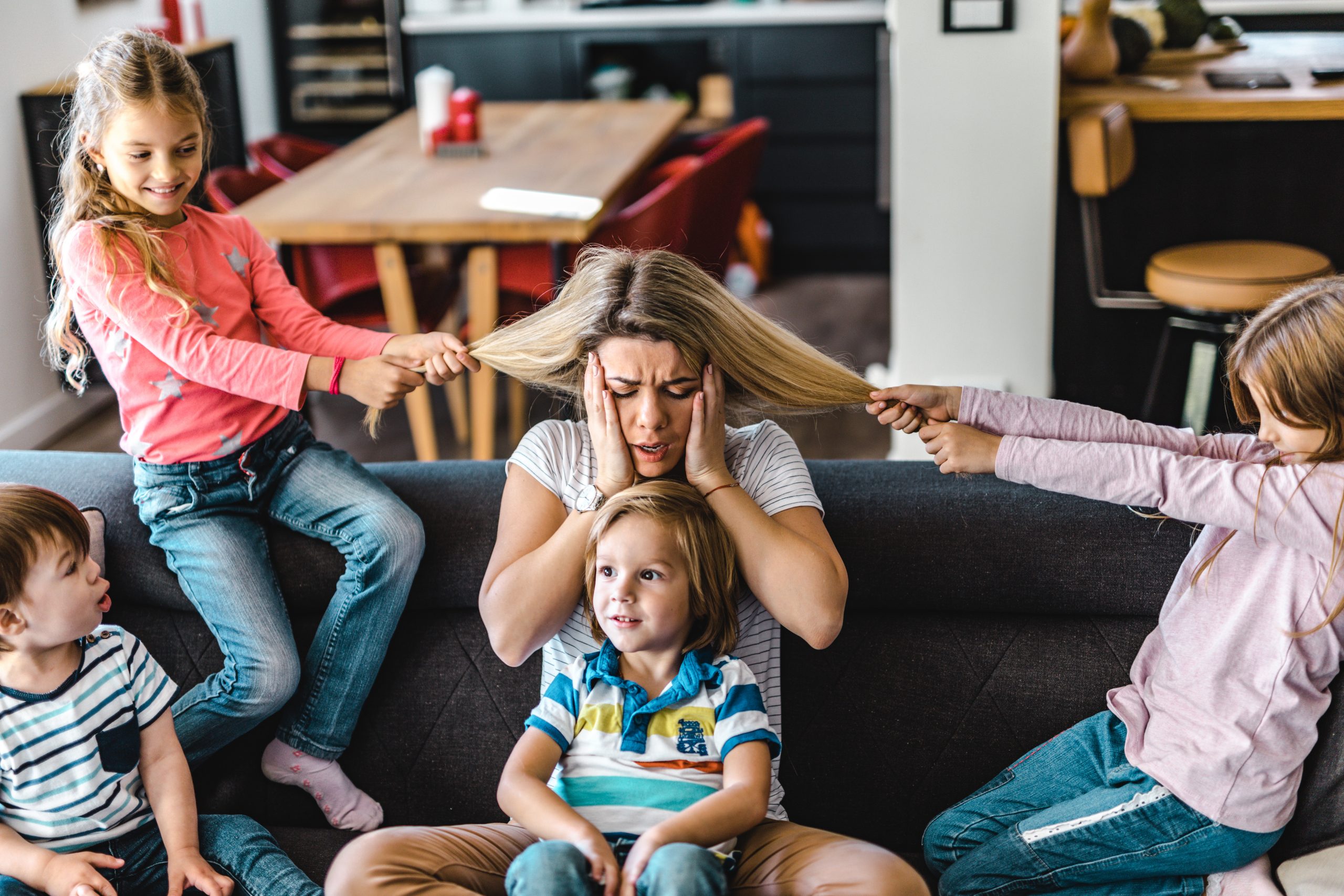 Small kids spending time with their frustrated nanny at home. Little girls are having fun while pulling her hair.