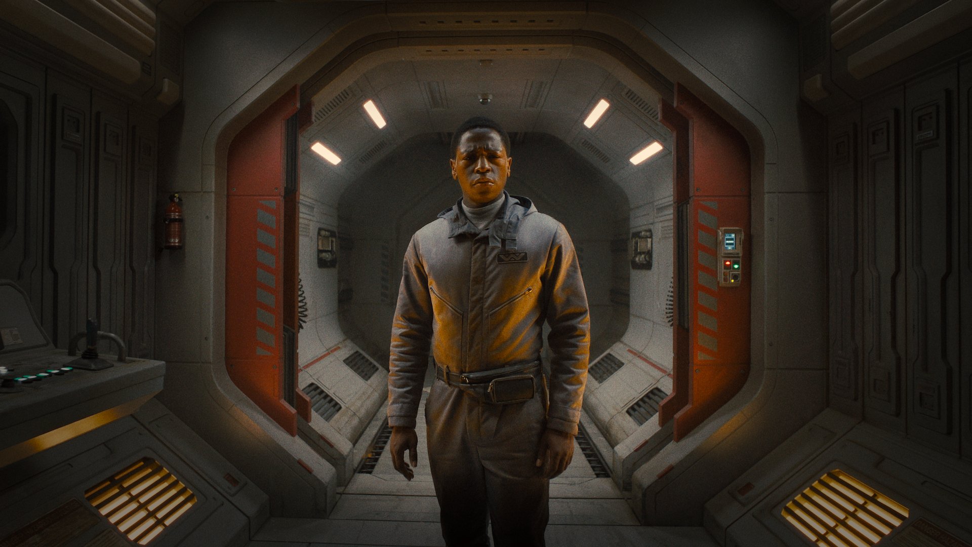 A man in a spacesuit stands in a spaceship hallway looking worried.