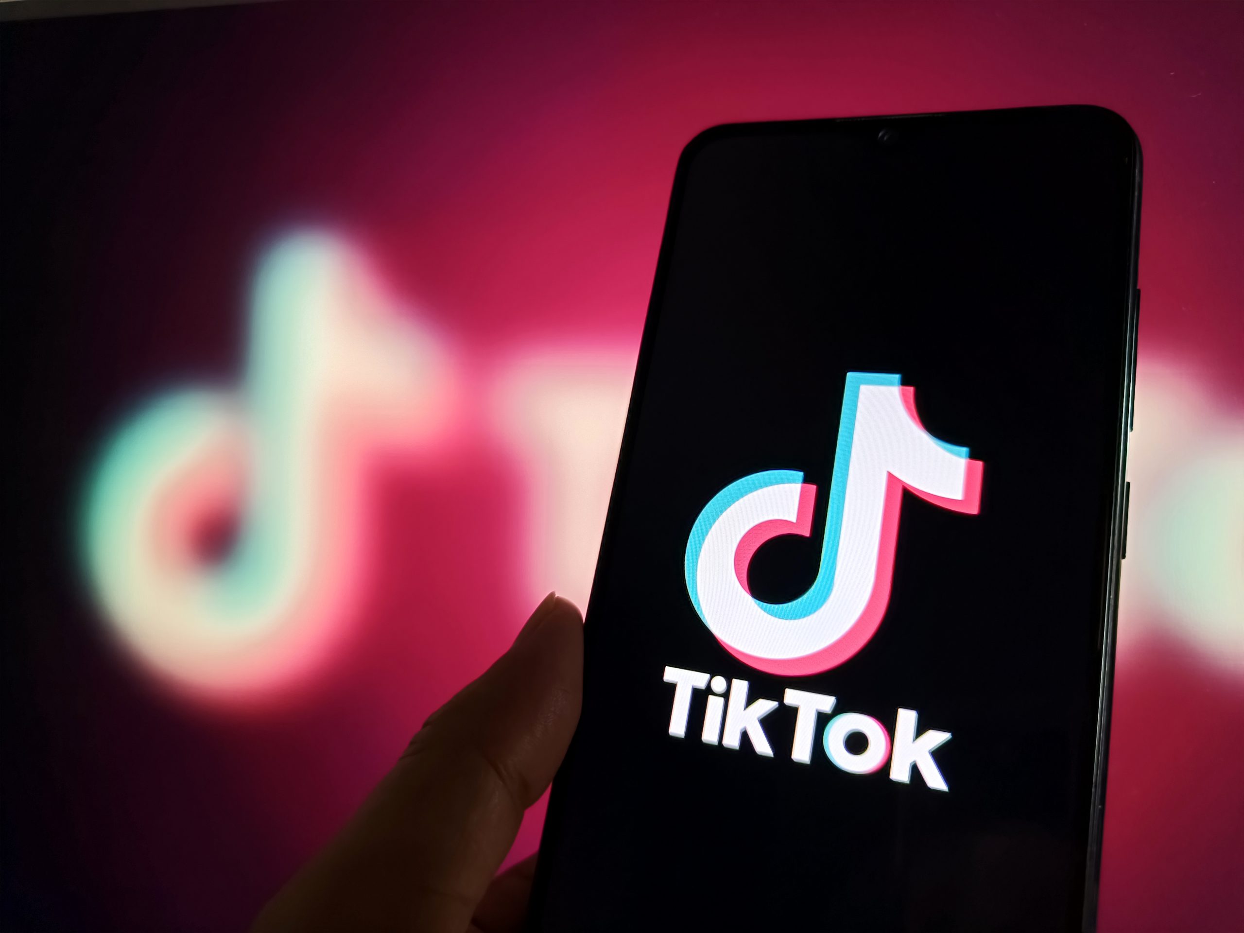 A phone displaying the TikTok logo in front of a blurry pink-hued TikTok logo.