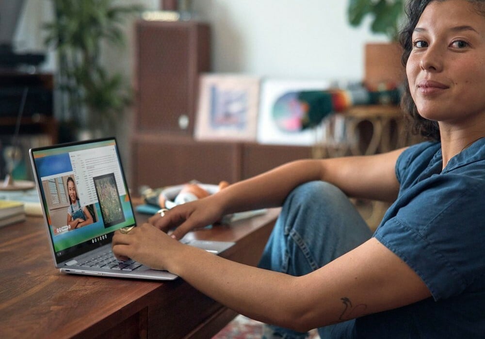 a person sits at a desk with a laptop in front of her while slightly smiling toward the camera