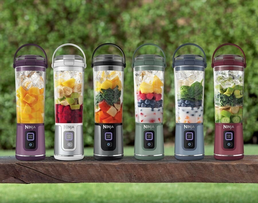 a lineup of ninja portable blenders that are various colored and filled with various smoothie ingredients, sitting in each blender unblended