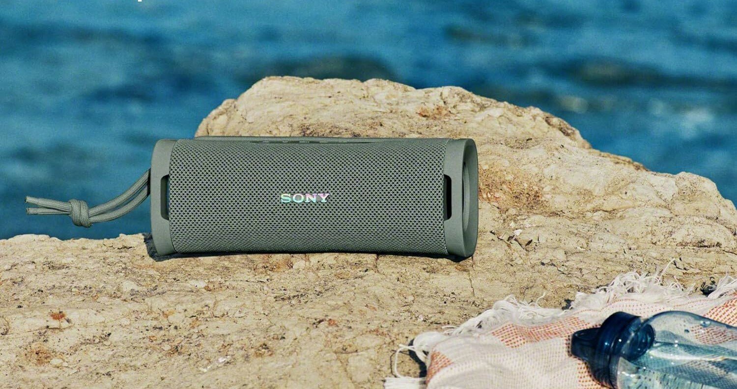 a portable sony bluetooth speaker sits on a towel atop a rock at the beach