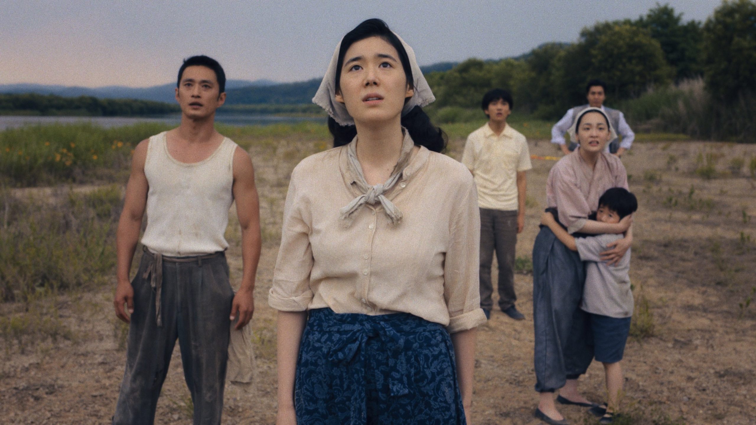 The Baek family stands in a brown field, looking up at the sky in worry.