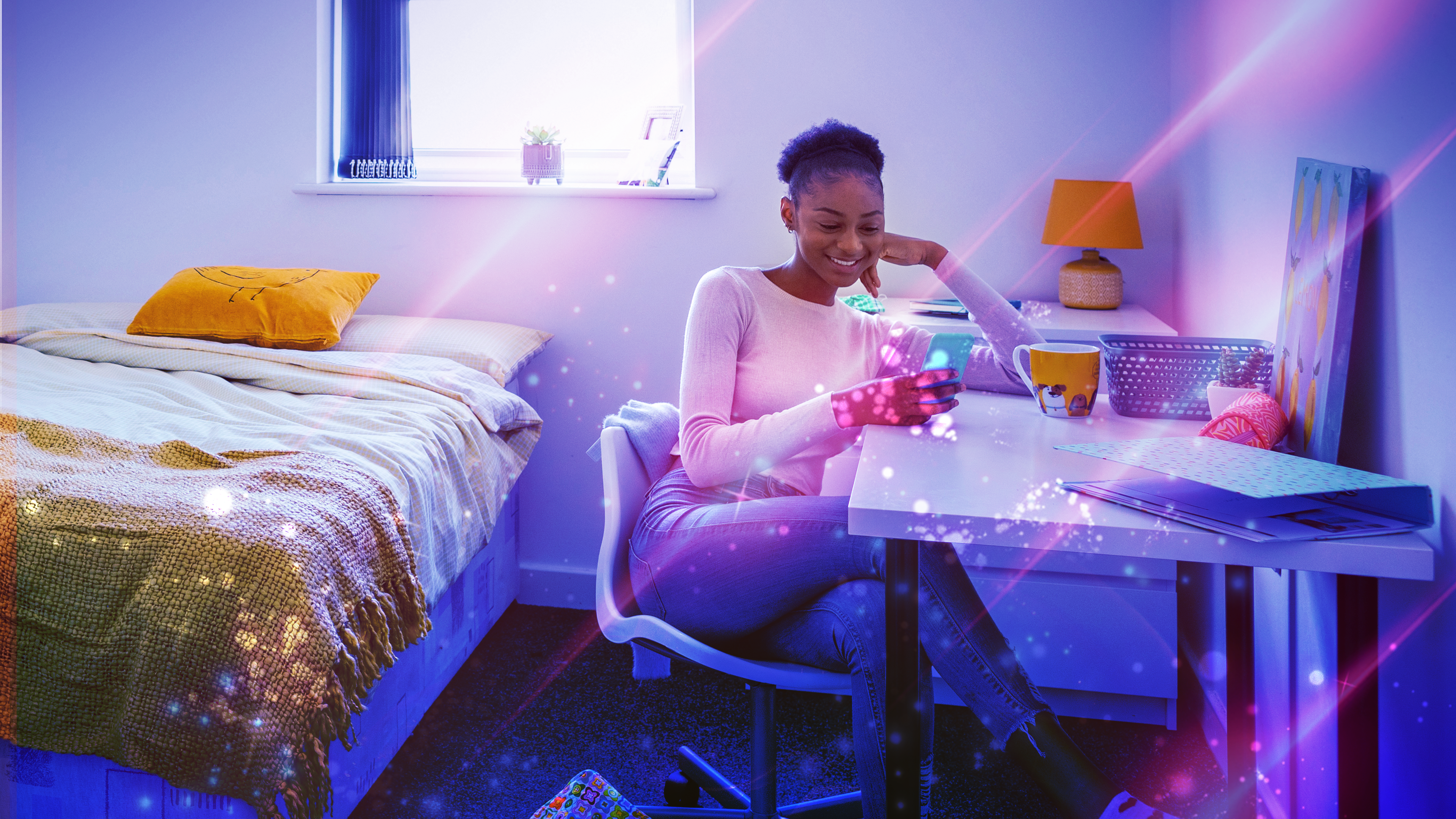 A young women in her dorm room surrounded by tech. 