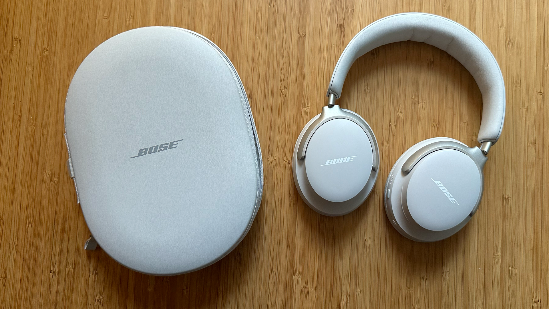 A pair of Bose QuietComfort Ultra headphones and case on a wooden table