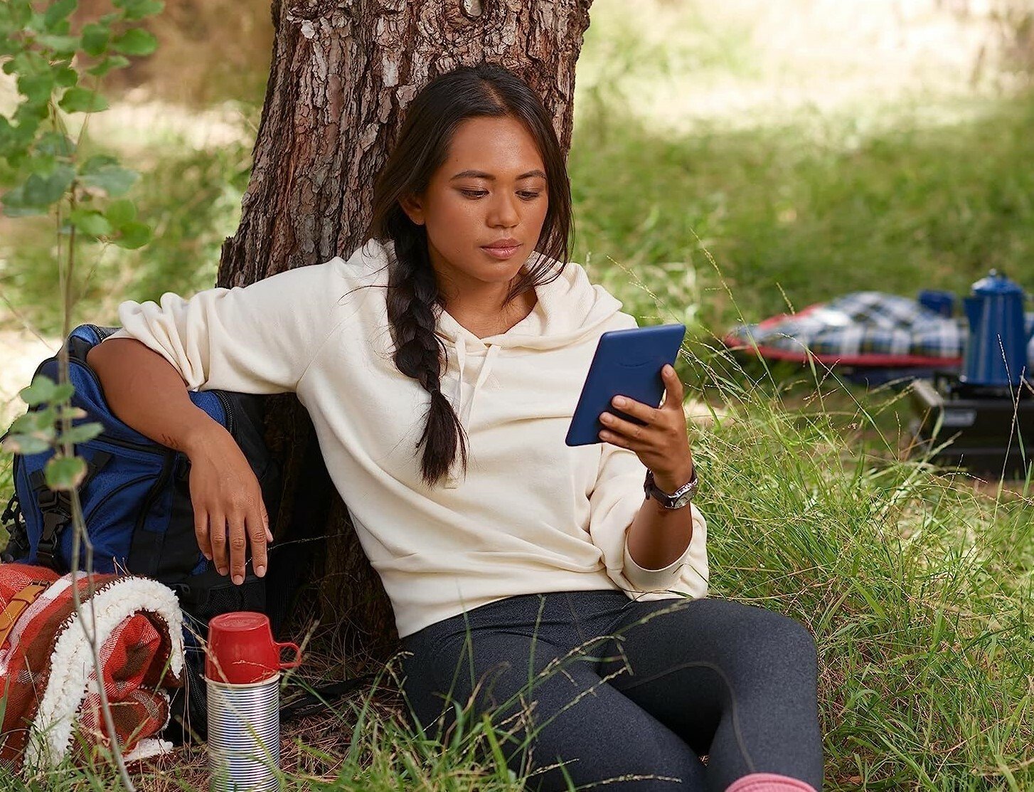 A girl sits outside and reads on her Amazon Kindle 