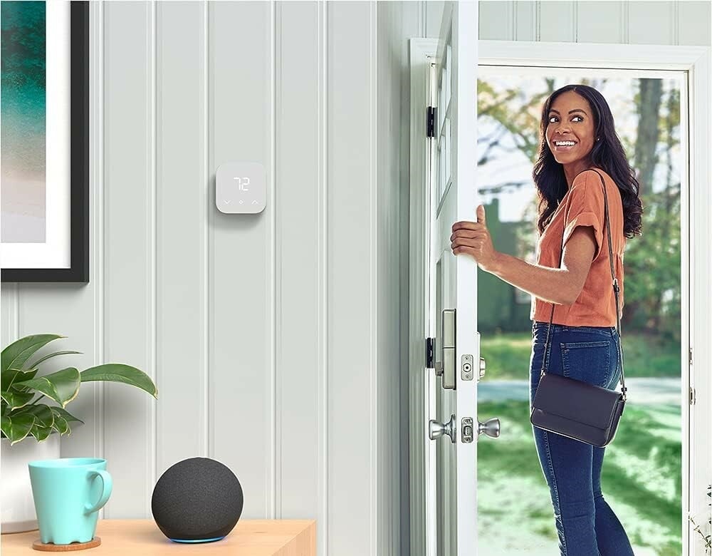 a person leaves the front door of a house, while looking back inside and smiling. On the wall is an amazon smart thermostat