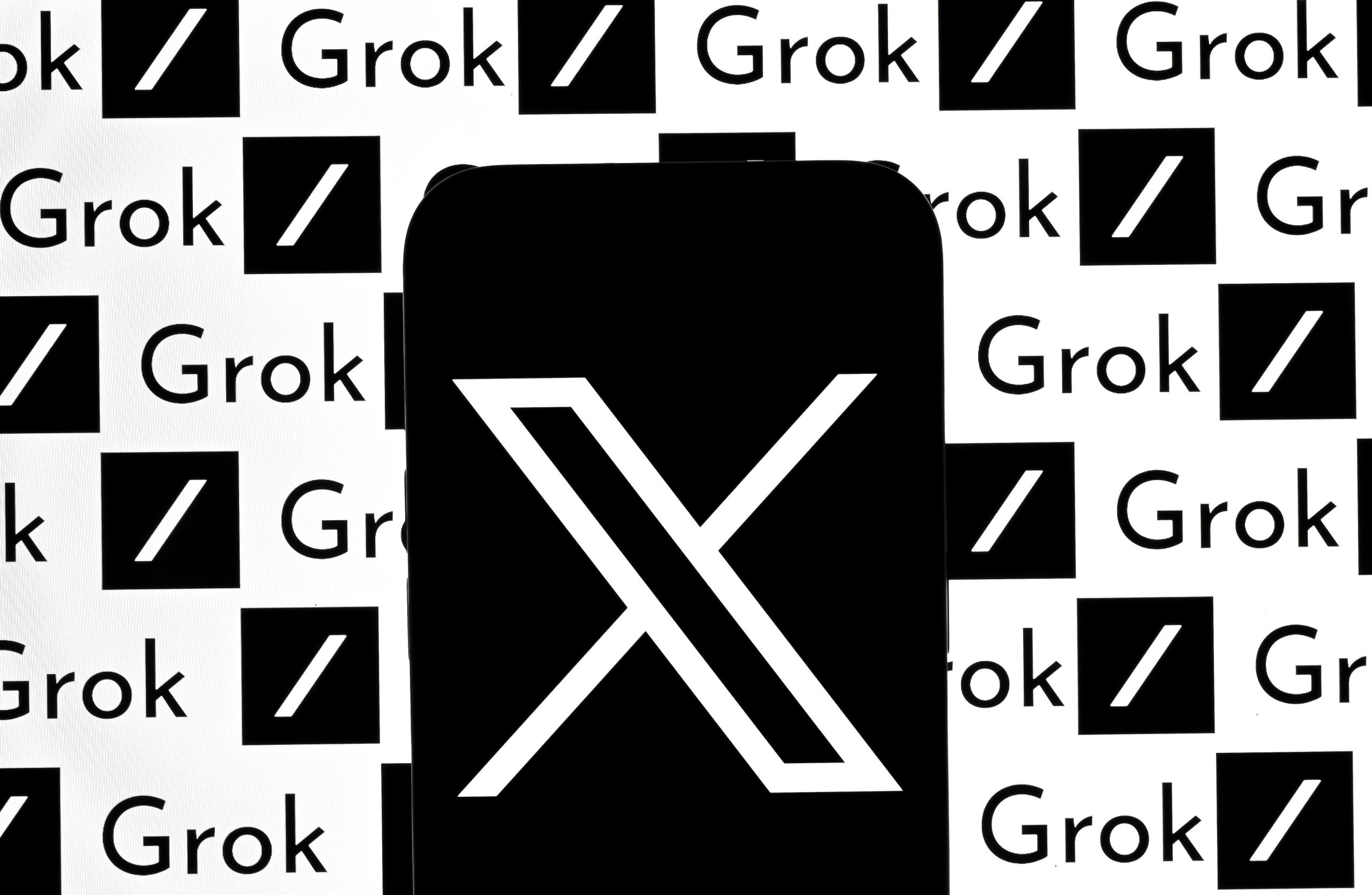 A phone displaying the X logo in front of a screen displaying the Grok logo.