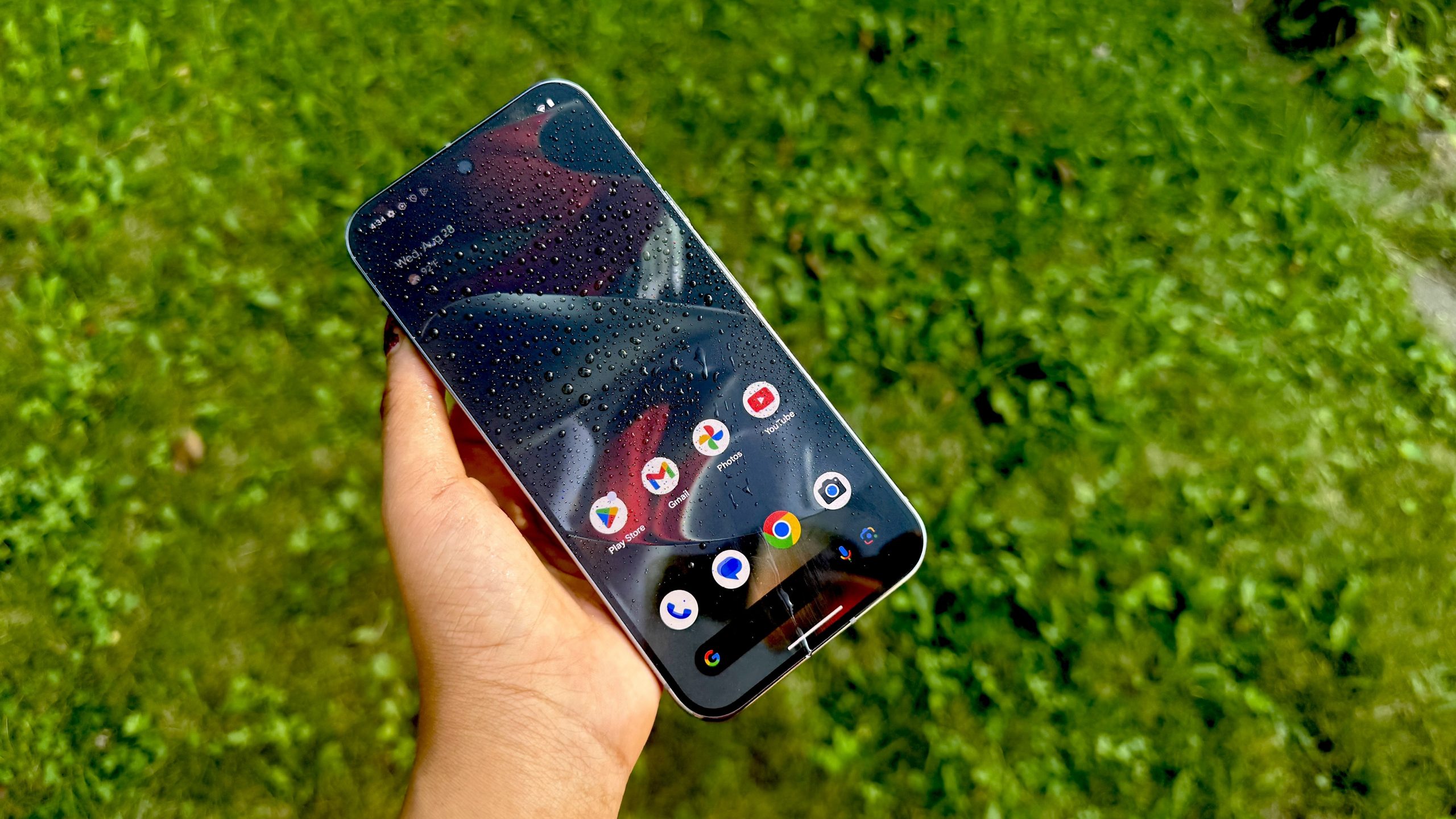 Google Pixel 9 Pro XL with water droplets on its screen with grass in the background