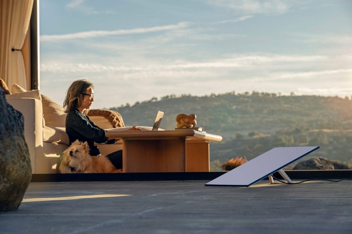 a starlink wifi satellite sits on a wooden deck while a woman works on a laptop in the background with her dog