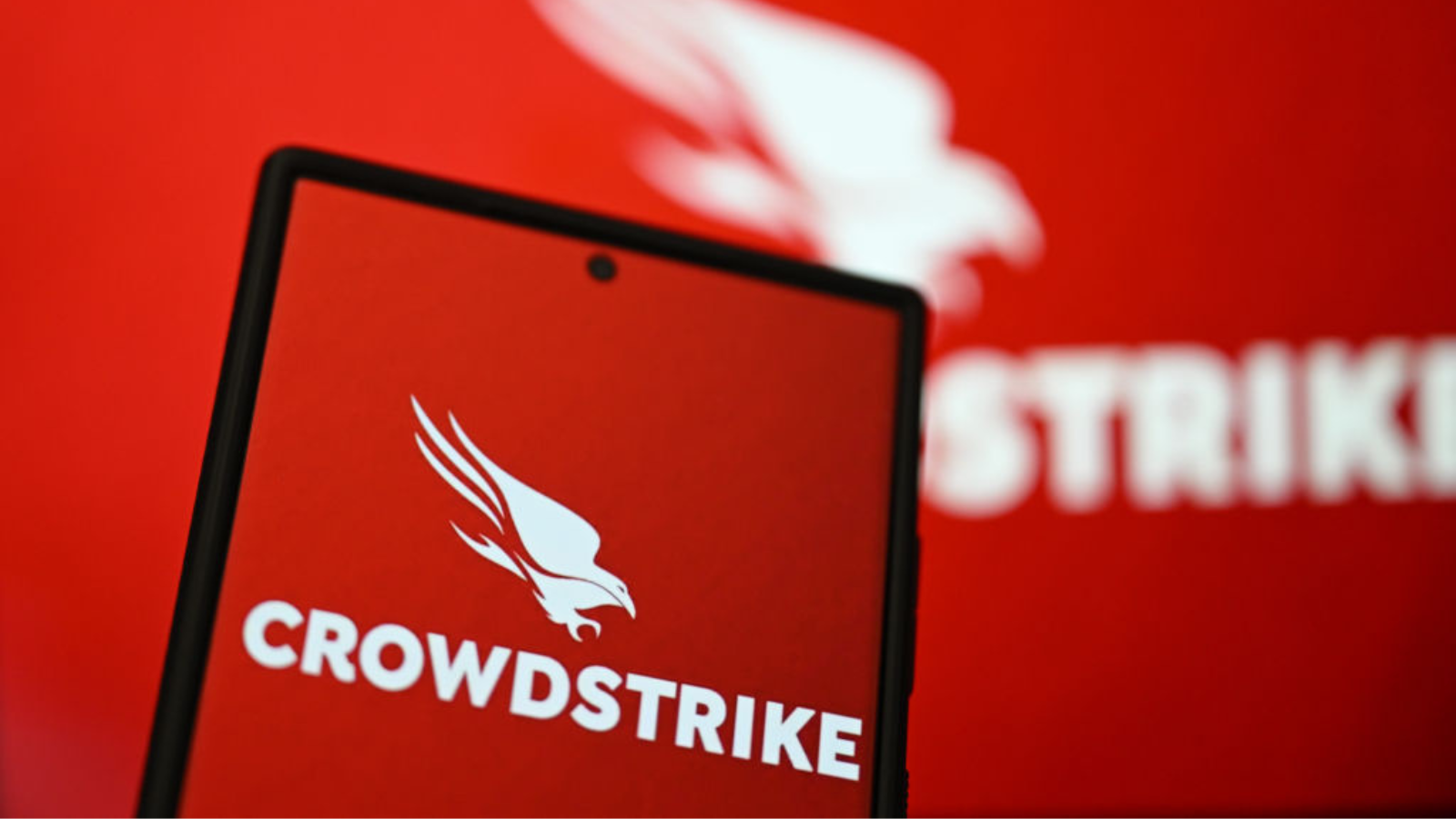 The CrowdStrike logo on phone screen is displayed in front of CrowdStrike logo on laptop screen.