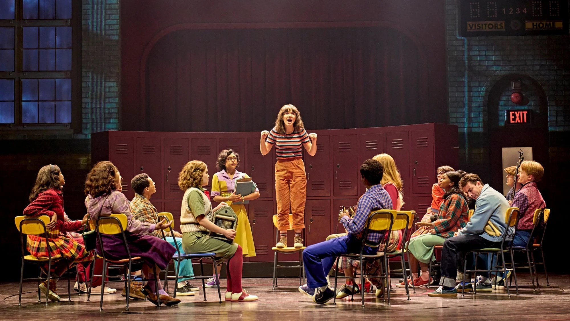 The cast of the Stranger Things play onstage during a high school scene.