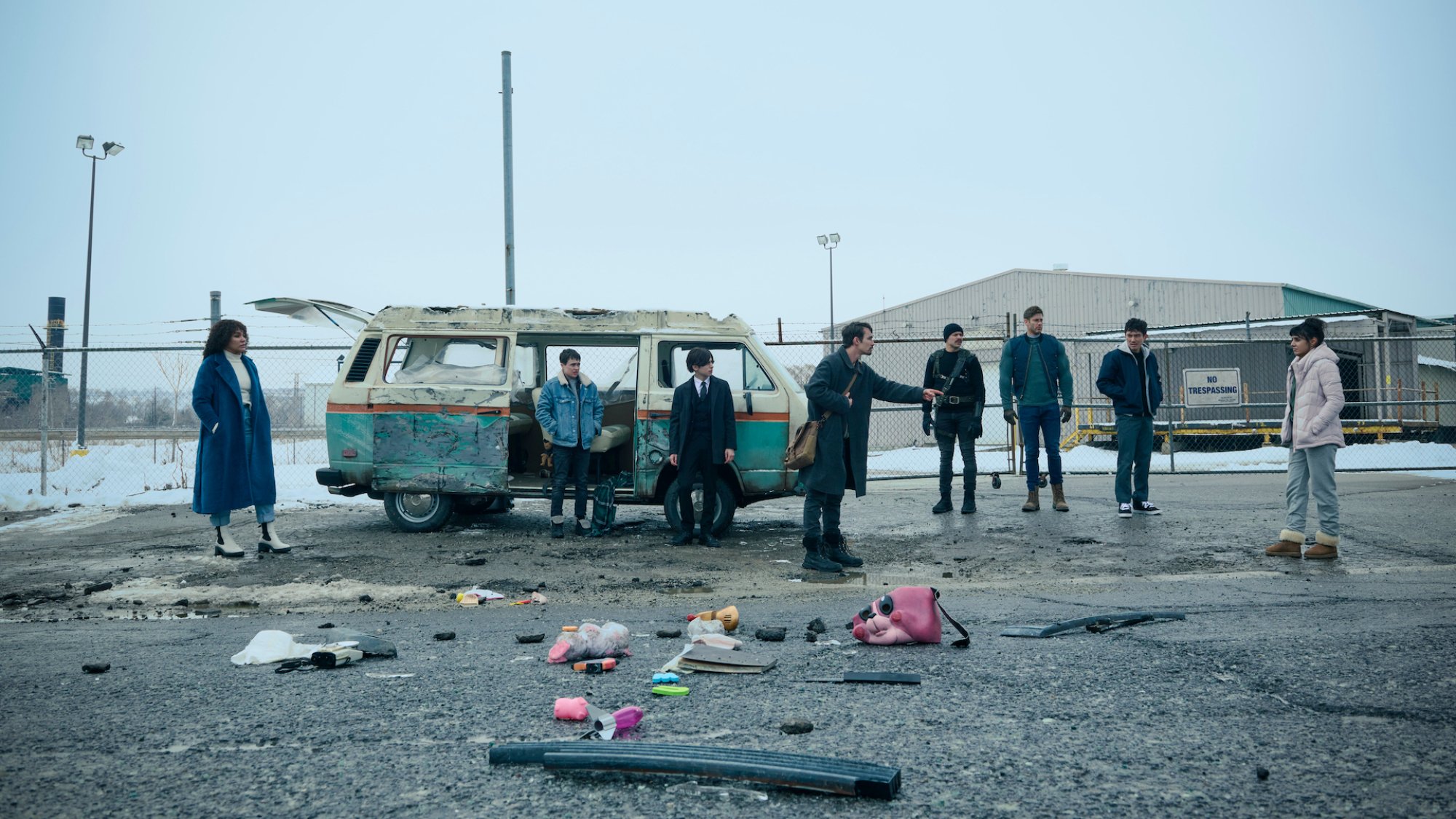 The cast of "The Umbrella Academy" stands beside a van in a vacant lot.