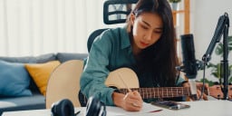 A woman writing with guitar in hand