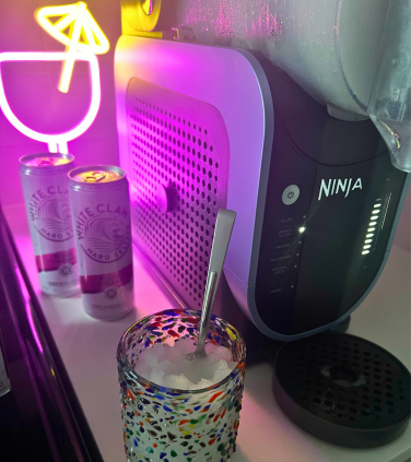 Glass of frozen spiked seltzer on countertop with Ninja Slushi machine and White Claw cans in background