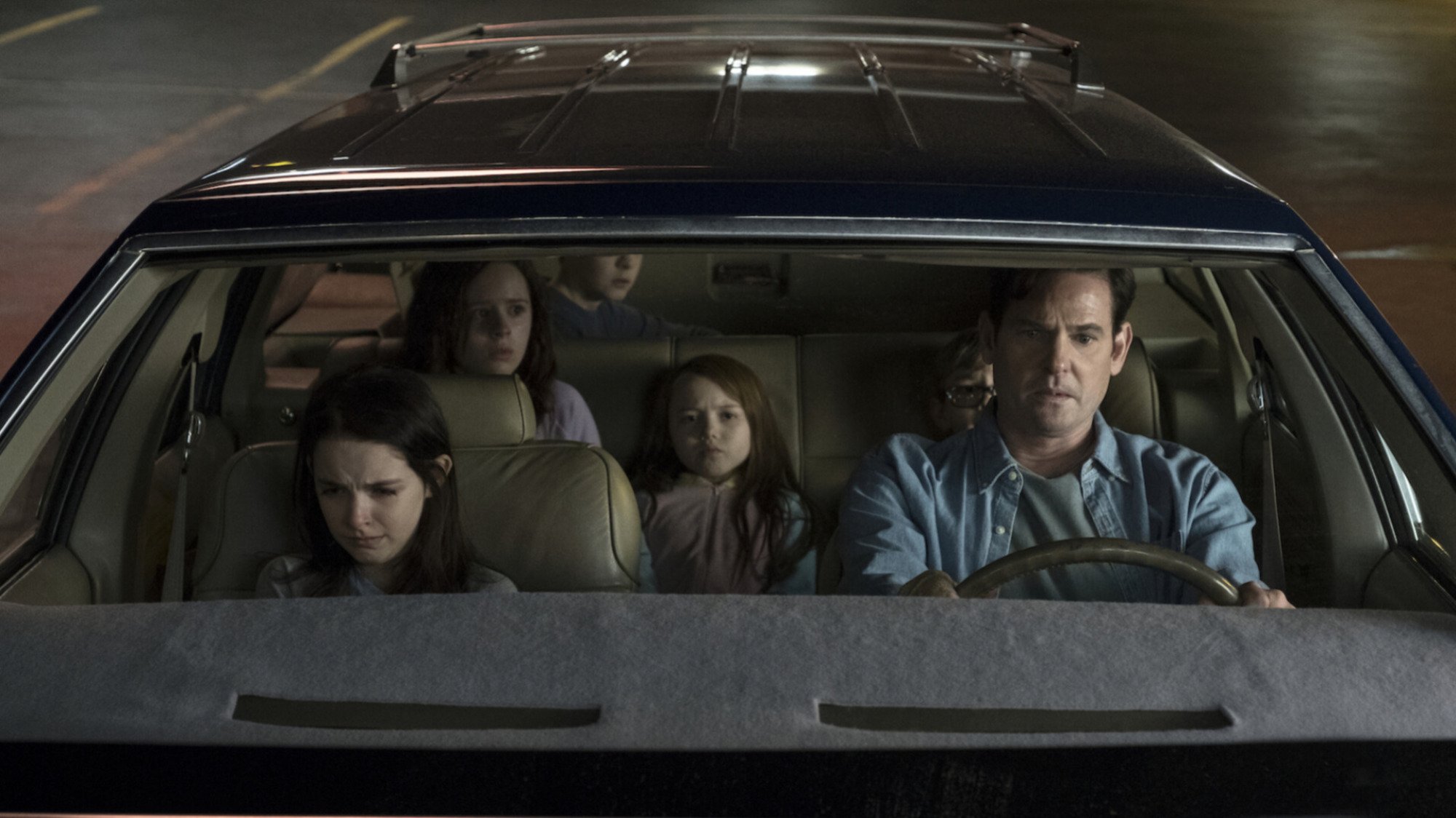 A family sit in their car looking scared. 