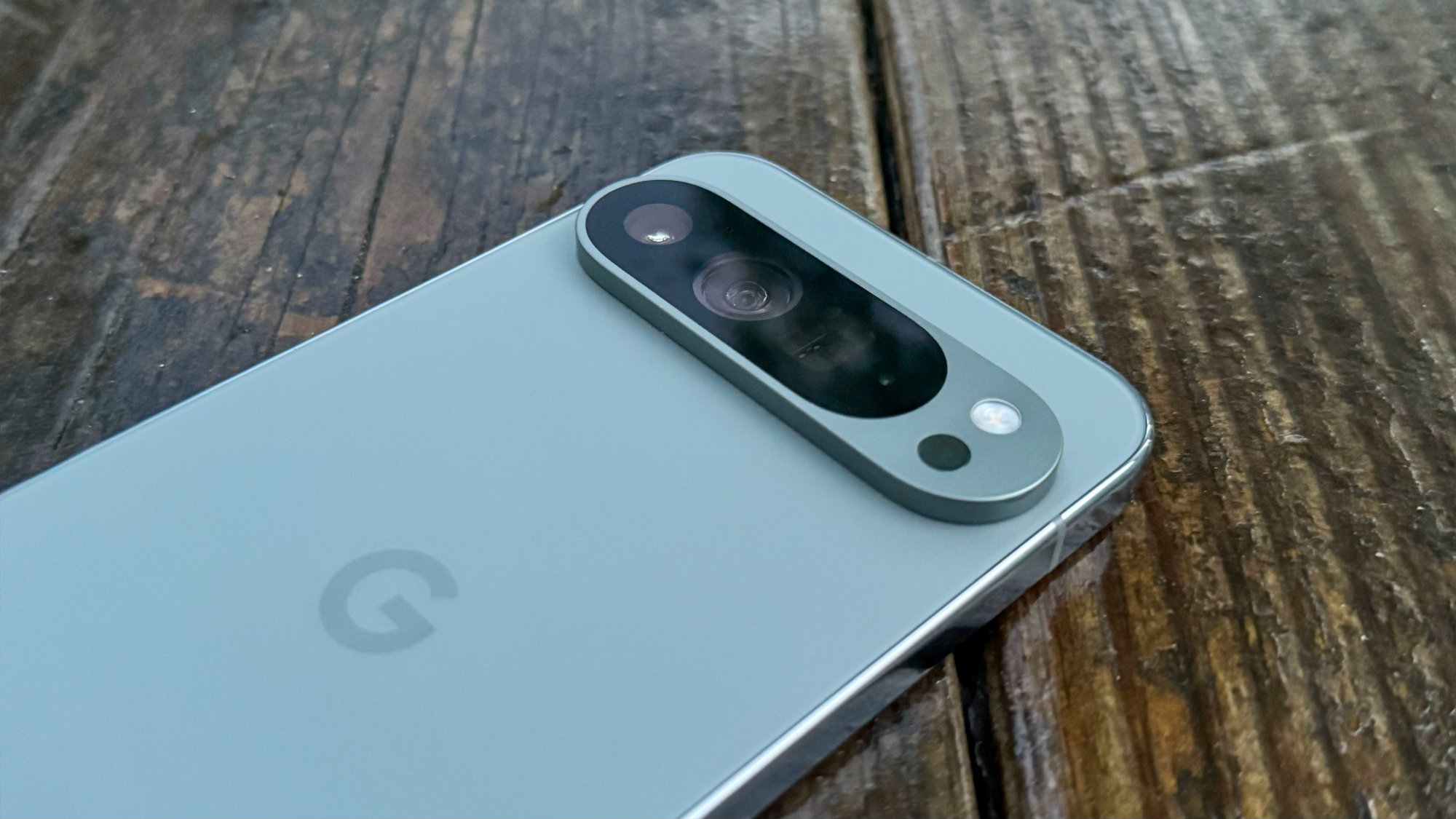 A close up of the Google Pixel 9 Pro XL on a wooden surface, screen facing down so the back camera is visible.