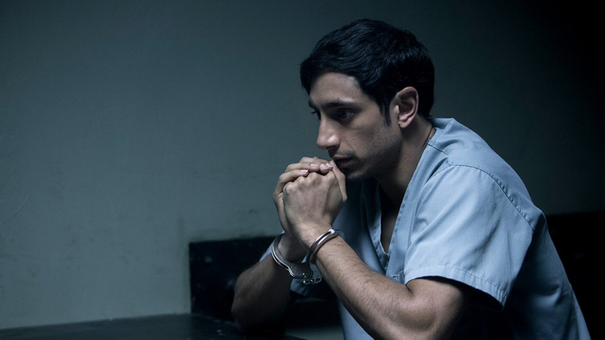 A man in cuffs sits in an interrogation room. 