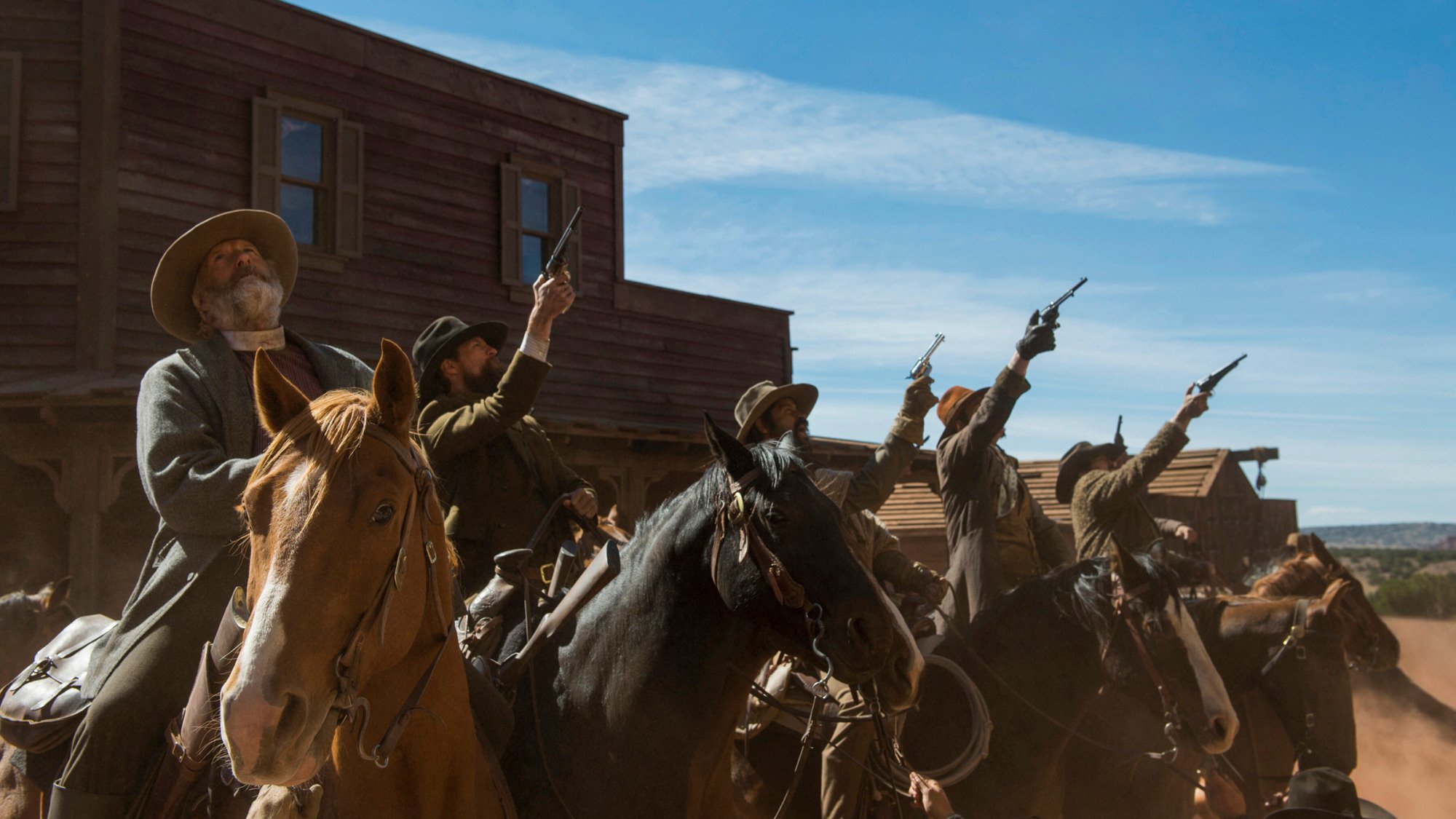 A group of cowboys on horses hold their guns up to the sky. 