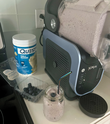 Bluberry milkshake with container of strawberries, protein powder, and Ninja Slushi in background