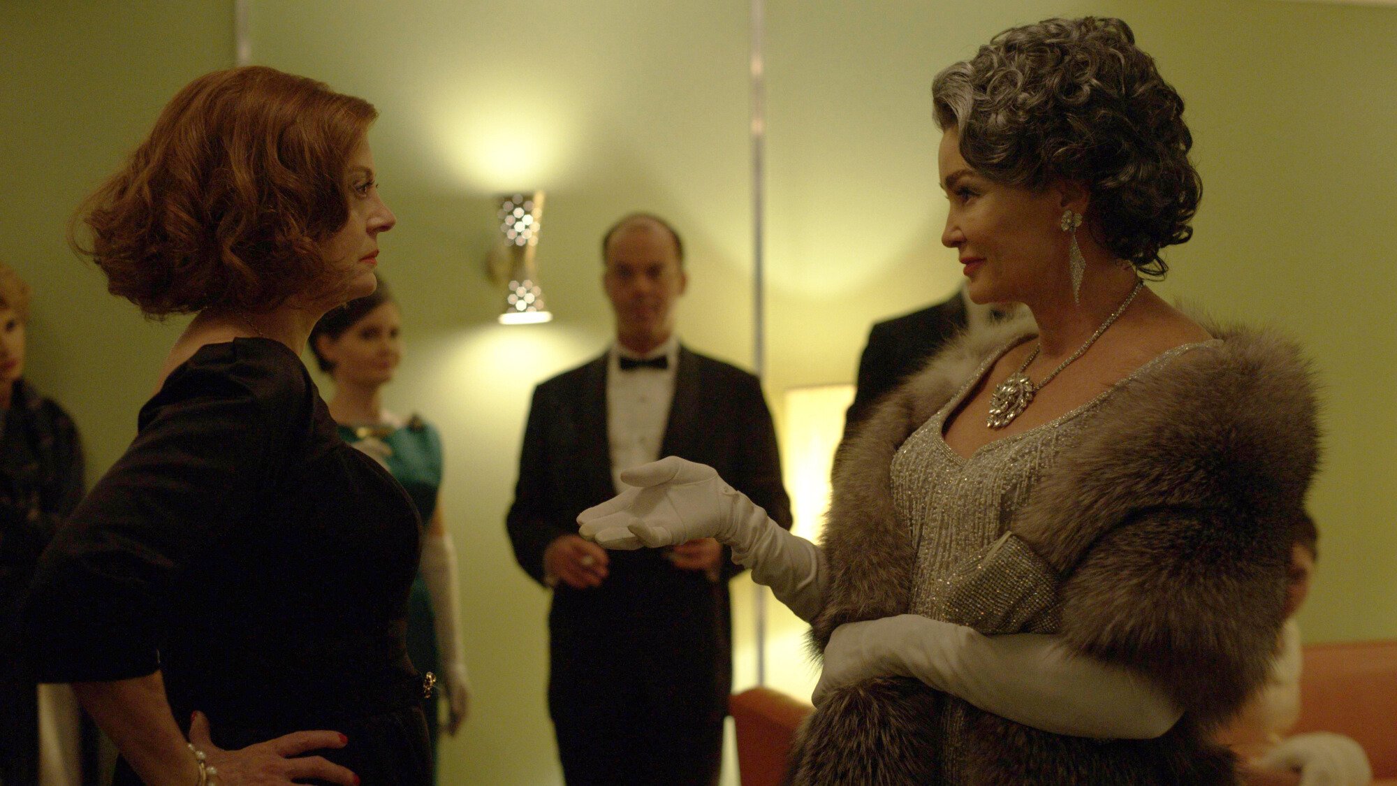 Two women wearing gowns greet each other at a party. 