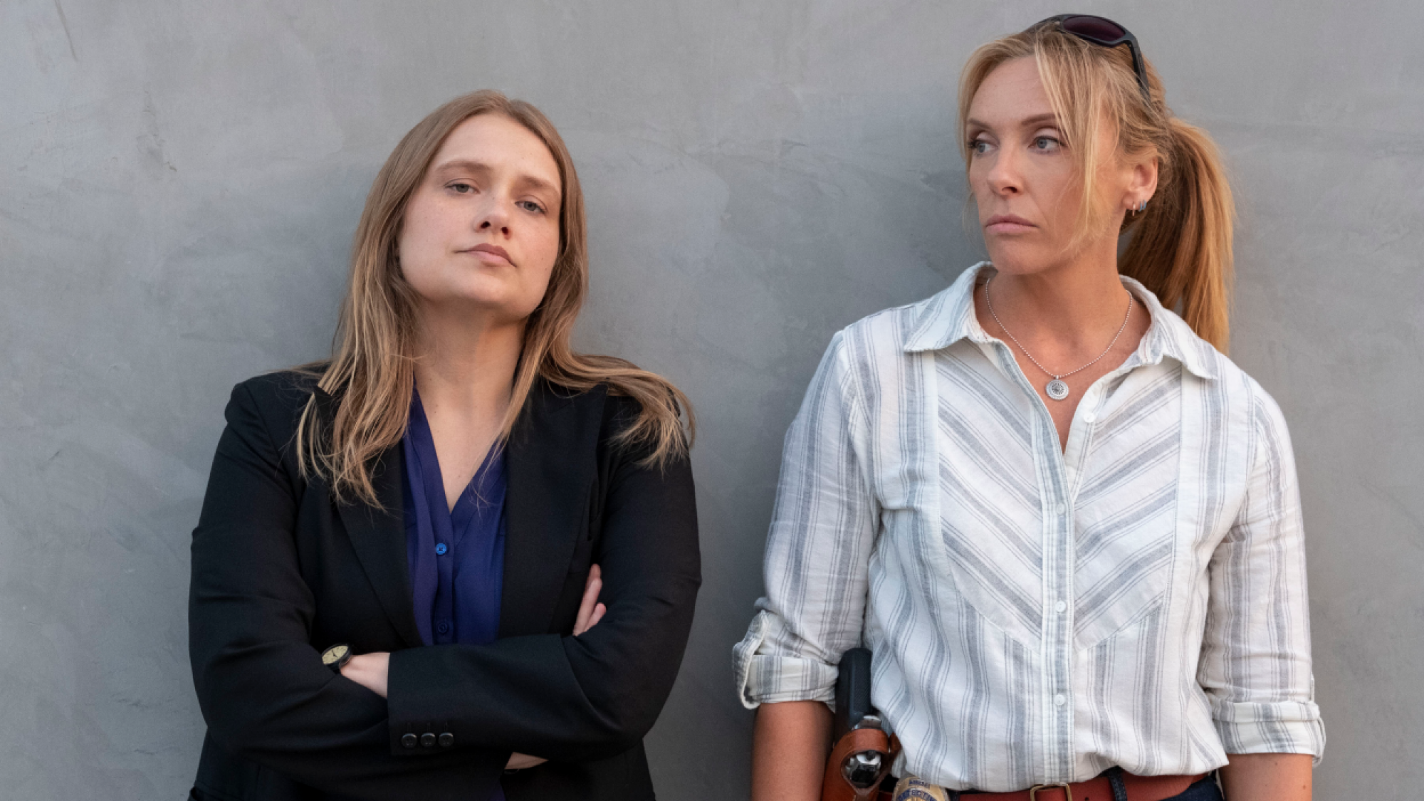 Two women lean on a wall. 