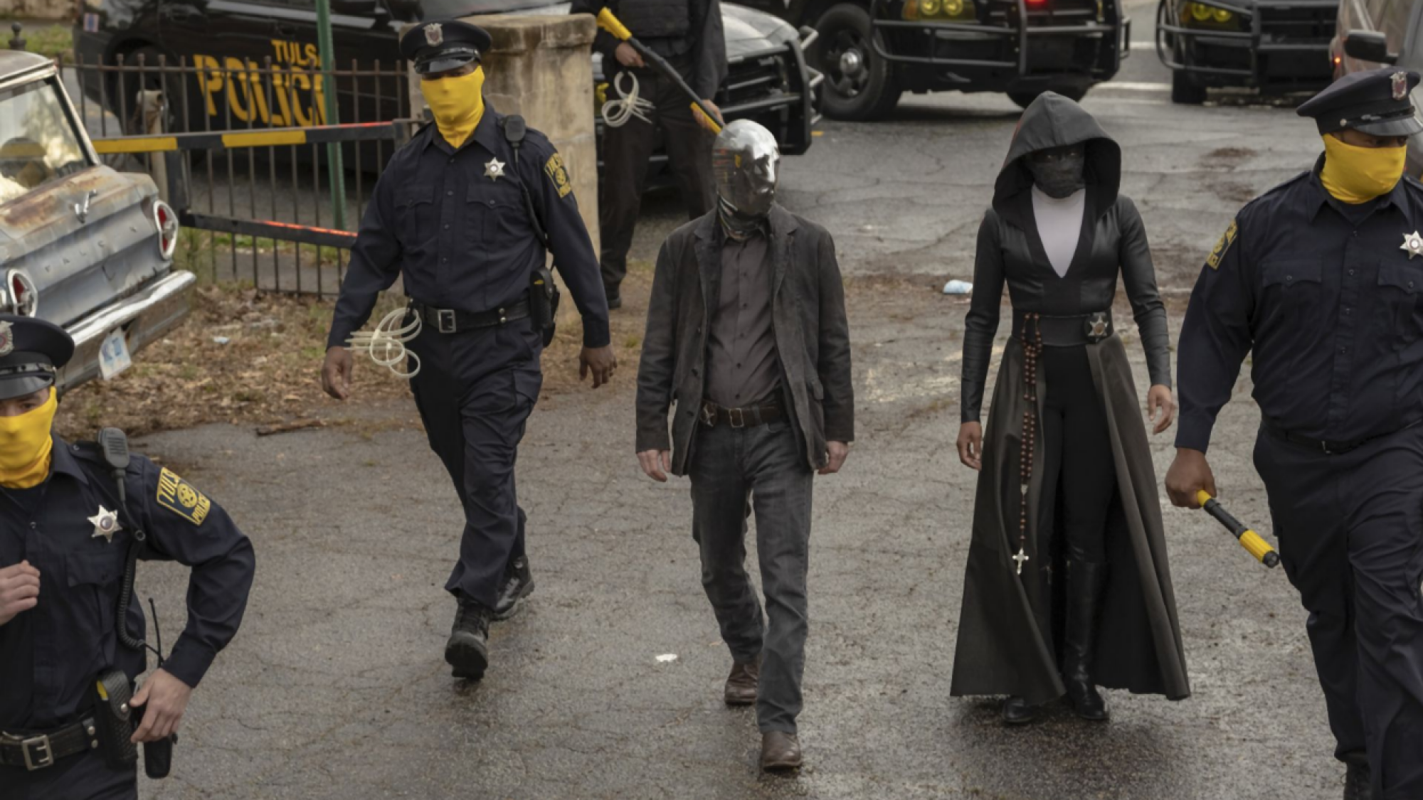 Police escort two people wearing masks. 