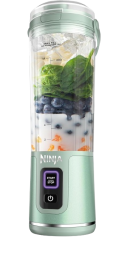 a pale green ninja blender on a white background. Inside of the blender are blueberries, spinach and milk