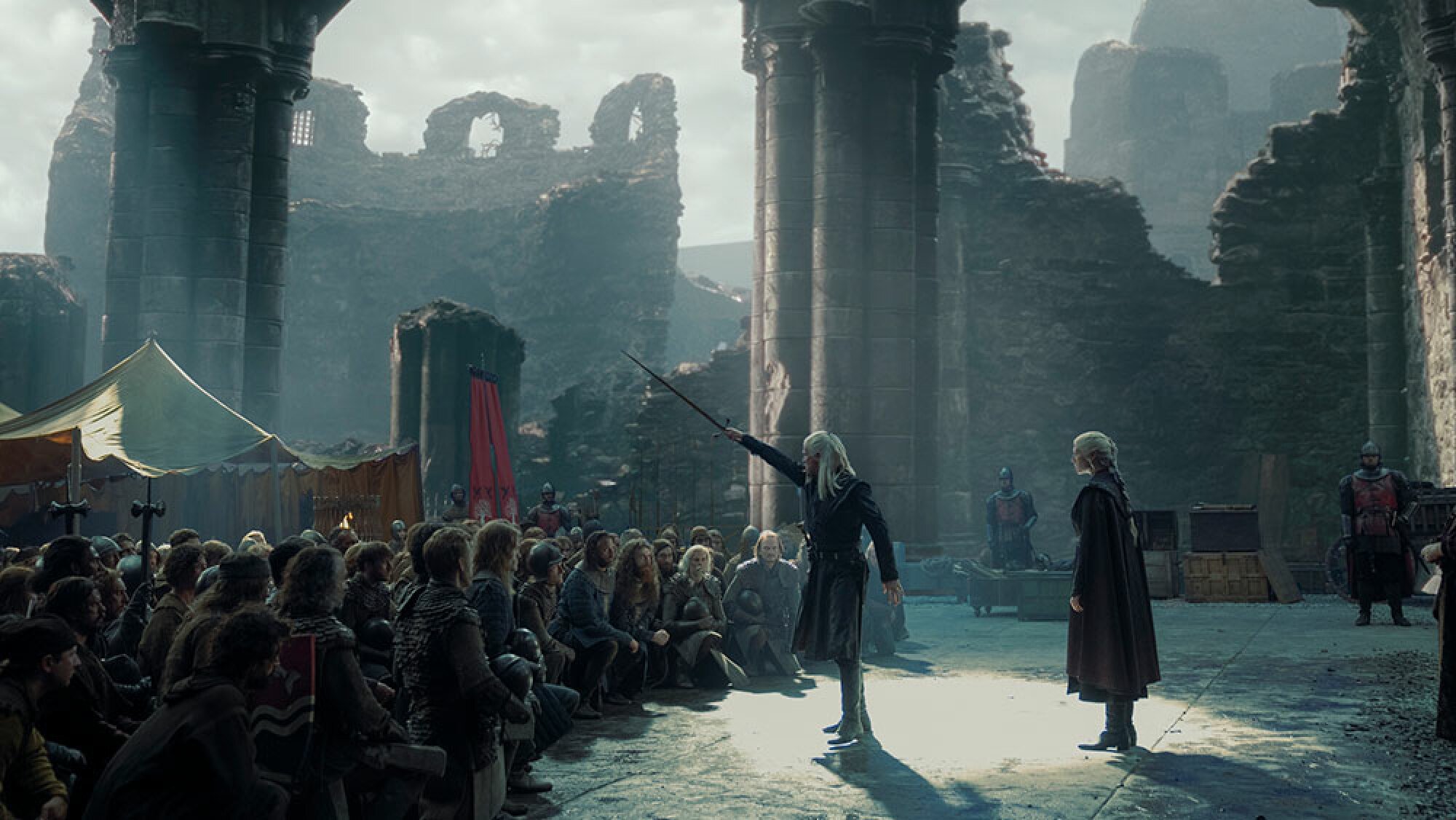 A man raises his sword in front of an army in the ruins of a castle, while a woman beside him watches on.