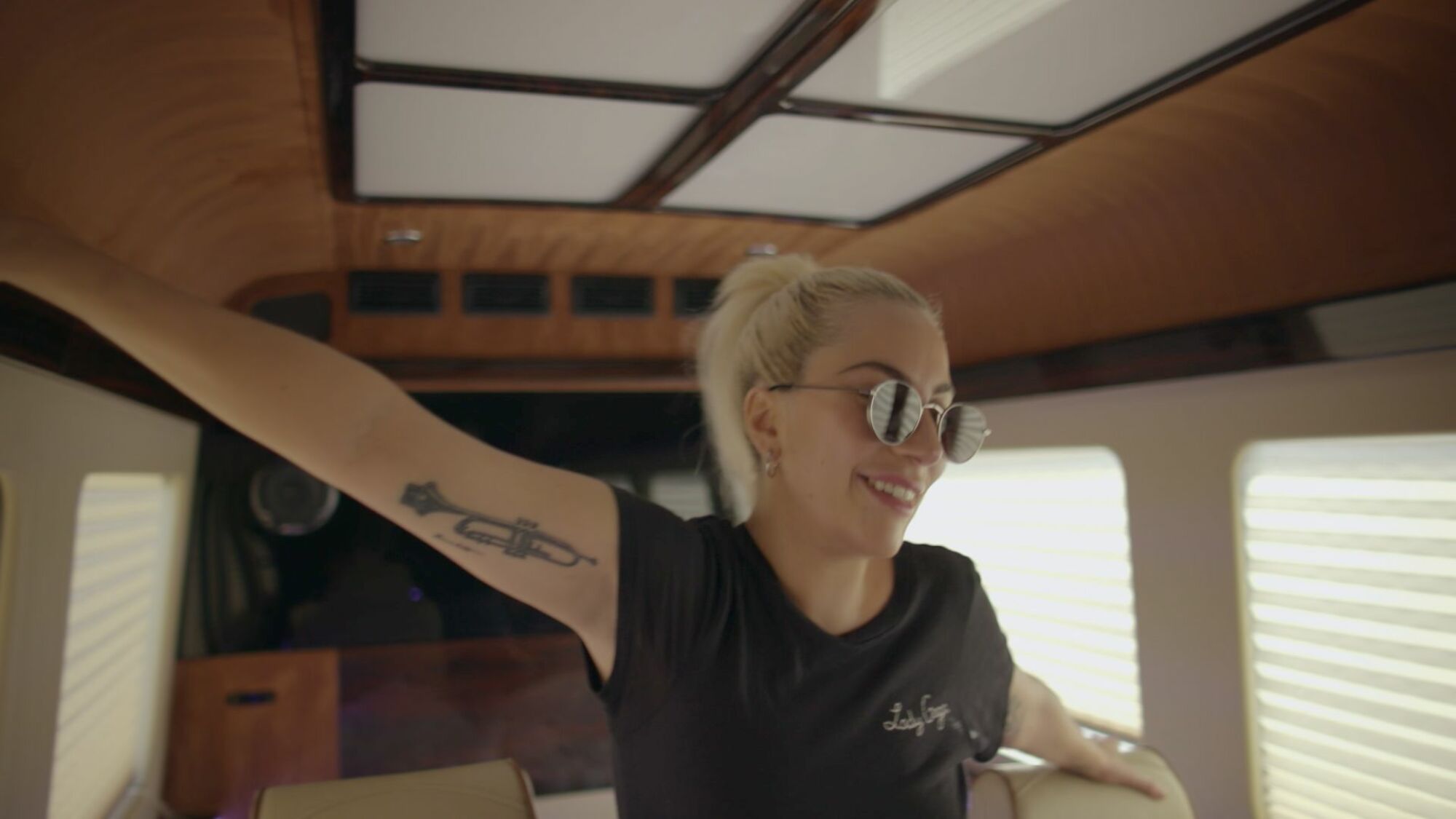 Lady Gaga stands in her tour trailer with arms outstretched. 